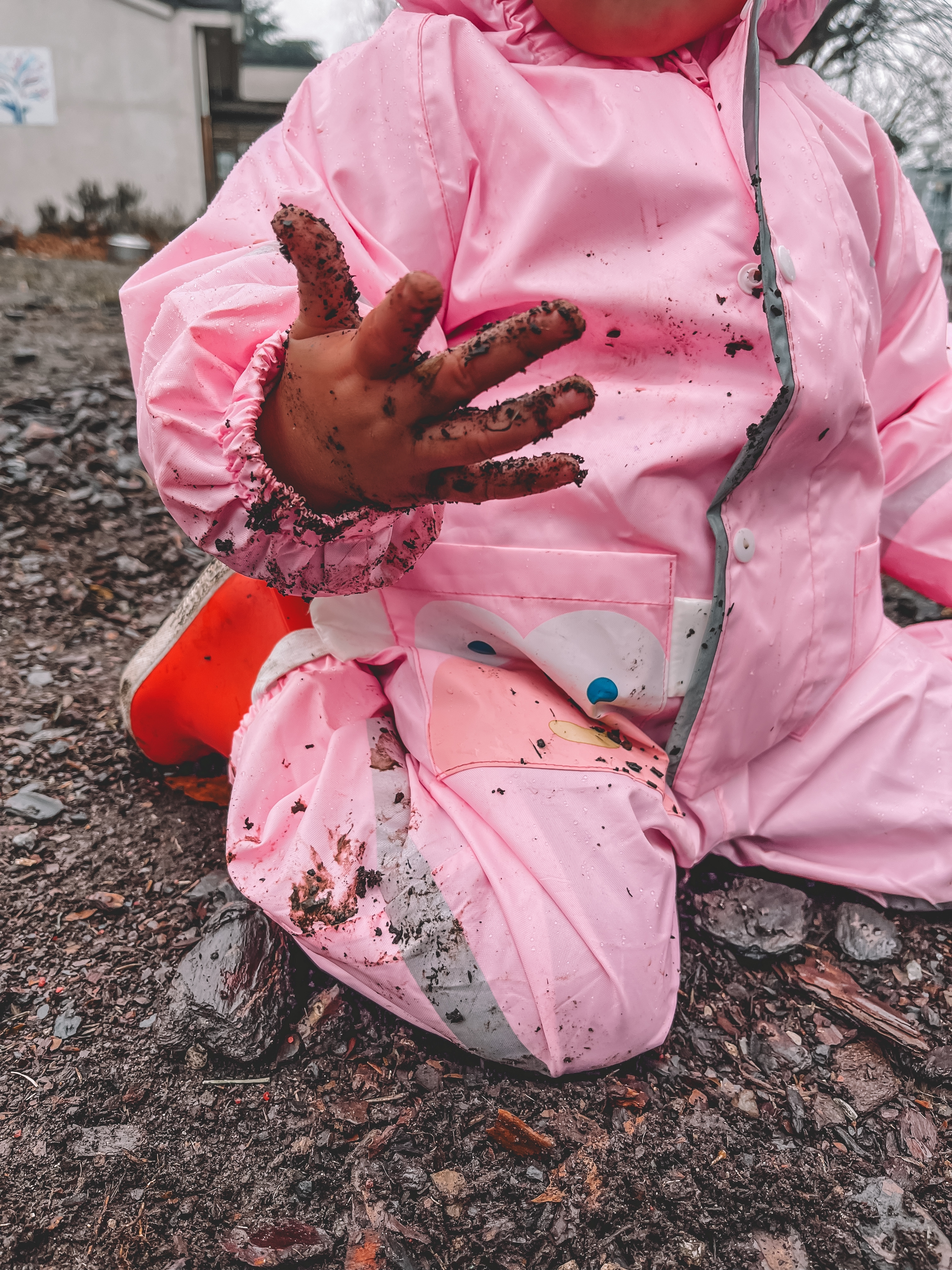 child with muddy hands wearing pink rainsuit